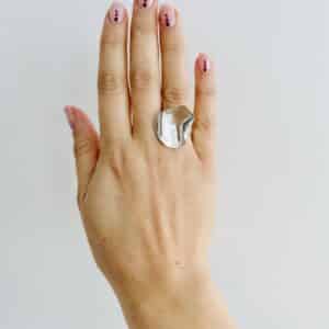 A hand wearing a shiny silver ring shaped as a rose petal.