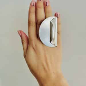 A hand wearing a handmade silver ring shaped as a big coin with on side folded.