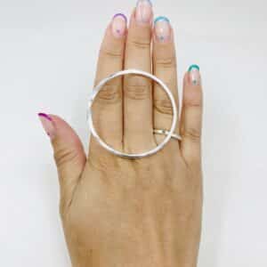 A hand with rainbow coloured nail polished wearing a big silver ring shaped as a twisted circle